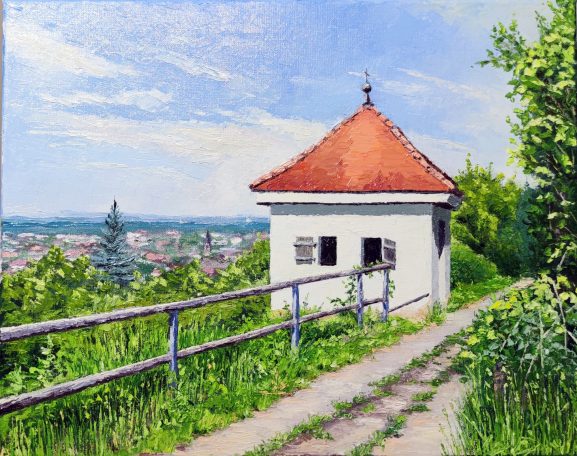 Weißes, schlichtes Gebäude mit rotem Dach, umgeben von grüner Vegetation und weitem Ausblick.